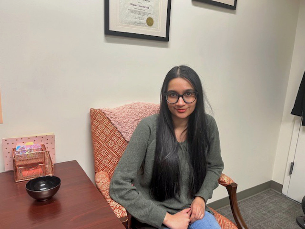 a smiling women sitting in office with framed certificate in background